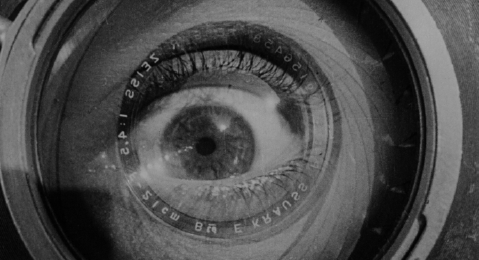Black-and-white image for Vertov's film "Man with a Movie Camera" showing the reflection of a man's eye in the lens of a camera. 