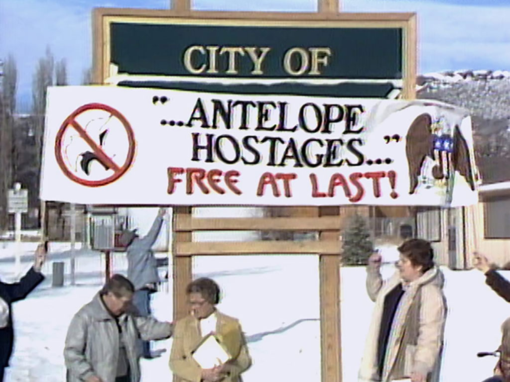 Three people standing beneath a large banner sign that says "... Antelope Hostages ... Free at Last."